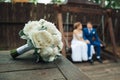 In focus wedding bouquet on a wooden floor against a background of kissing newlyweds. Wedding concept