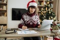 Focus on woman hand with pen in Santa hat making notes on draft paper document