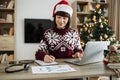 Focus on woman hand with pen in Santa hat making notes on draft paper document
