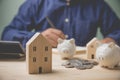 Focus at wood house model with coins stacking and piggy bank. Businessman recording accounting using calculator calculate for buy