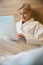 Focused adult caucasian businesswoman typing on laptop on bed in hotel room Royalty Free Stock Photo