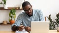 Focused African American businessman using laptop, writing notes