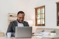 Focused african american businessman working with laptop documents in office holding papers preparing report analyzing Royalty Free Stock Photo