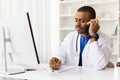 Focused African American doctor taking notes during phone conversation at work desk Royalty Free Stock Photo
