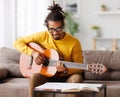 Focused african american male musician with classic acoustic guitar reading sheet music on paper Royalty Free Stock Photo