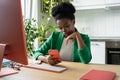 Focused African American woman holding phone reading business press sits at computer desk in office