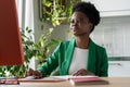 Focused African American woman sits at computer desk holding mouse in hand and looking at monitor Royalty Free Stock Photo