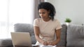 Focused African American woman using laptop, making notes