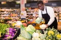 Focused African man working in organic food store, putting fresh vegetables in boxes on showcase