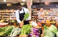 Focused African man working in organic food store, putting fresh vegetables in boxes on showcase