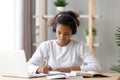 Focused african african teen girl wearing headphones writing notes studying
