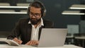 Focused Arabian male Indian businessman wear headphones ethnic business man studying working in office with laptop Royalty Free Stock Photo