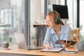 Focused Asian businesswoman wearing headphones is taking notes in a notebook while watching a webinar video course Royalty Free Stock Photo