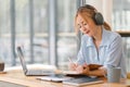 Focused Asian businesswoman wearing headphones is taking notes in a notebook while watching a webinar video course Royalty Free Stock Photo
