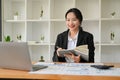 Focused Asian female accountant looking at laptop screen, taking notes on her book Royalty Free Stock Photo