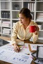 Focused Asian female accountant sipping coffee and analyzing business financial data Royalty Free Stock Photo