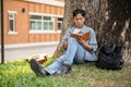 A focused Asian male student is reading a book or writing some ideas in a book under the tree Royalty Free Stock Photo