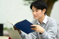 Focused asian man student reading interesting book while sitting on bench in city park. Education, lifestyle concept Royalty Free Stock Photo