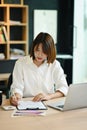 Focused asian woman employee working with laptop and checking financial reports on wooden office desk Royalty Free Stock Photo