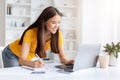 Focused Asian woman working on laptop and taking notes at home office Royalty Free Stock Photo