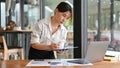 Female financial assistant looking the details on laptop screen and writing on clipboard Royalty Free Stock Photo