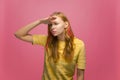 Focused attentive serious young woman looking far away with hand over head, searching on pink studio background