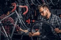 Focused attractive man in glasses is chainging wheel for bicycle at busy workshop
