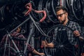 Focused attractive man in glasses is chainging wheel for bicycle at busy workshop