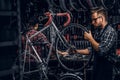 Focused attractive man in glasses is chainging wheel for bicycle at busy workshop