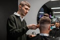 Focused barber cuts client hair with trimmer in barbershop