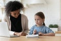 Focused biracial woman helping small child with study at home.