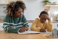 Focused biracial woman tutor give private educational lesson thoughtful child schoolboy at desk home