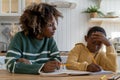 Focused biracial woman tutor give private educational lesson thoughtful child schoolboy at desk home