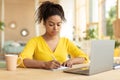 Focused black female student taking notes, watching online lecture on laptop, learning online at home, sitting at desk Royalty Free Stock Photo