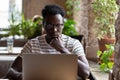 Thoughtful Black man watching educational webinar on laptop, studying, remotely online work in cafe. Royalty Free Stock Photo