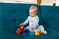 Focused blonde baby boy playing with toys while sitting on couch