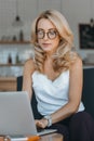 focused blonde woman in eyeglasses using laptop