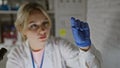 Focused blonde woman scientist examining a sample in a laboratory wearing gloves and lab coat