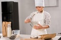 focused boy in chef hat and apron whisking eggs in bowl at table