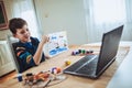 Boy painting and watching online course on laptop while practicing at home. Online training, online classes Royalty Free Stock Photo