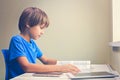 Focused boy reading a book. Tablet computer and mobile phone near to him at the table Royalty Free Stock Photo