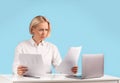 Focused business lady working with documents near laptop computer at her desk against blue background, copy space Royalty Free Stock Photo
