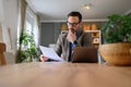Focused businessman in suit reading documents with laptop on desk while working from home office Royalty Free Stock Photo