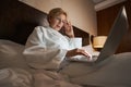 Focused businesswoman working remotely from comfortable hotel bed