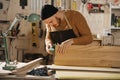 Focused carpenter in a watch cap grinding a piece of wood, in a big workshop