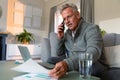 Focused caucasian senior man sitting on sofa, doing paperwork, making call and using laptop Royalty Free Stock Photo