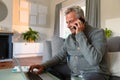 Focused caucasian senior man sitting on sofa, doing paperwork, using laptop and making call Royalty Free Stock Photo