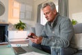 Focused caucasian senior man sitting on sofa, doing paperwork, using smartphone and laptop Royalty Free Stock Photo