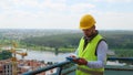 Focused Caucasian young man in uniform and helmet working on digital tablet while standing on construction site Royalty Free Stock Photo