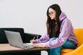 Focused caucasian young woman college student in eyeglasses studying with laptop distantly preparing for test exam writing essay Royalty Free Stock Photo